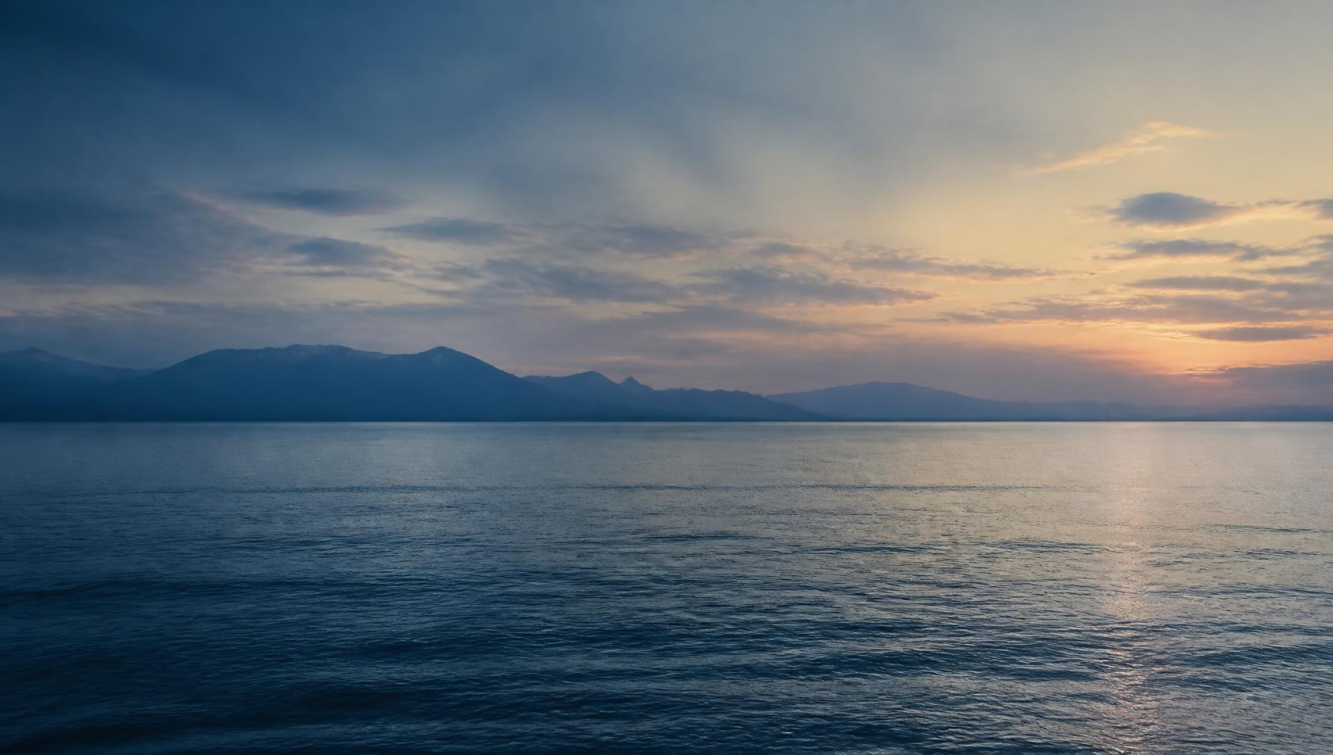 Calm ocean at dusk with a distant mountain silhouette